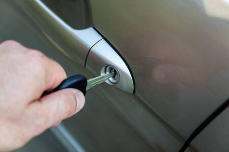man's hand opens the car door with a key.