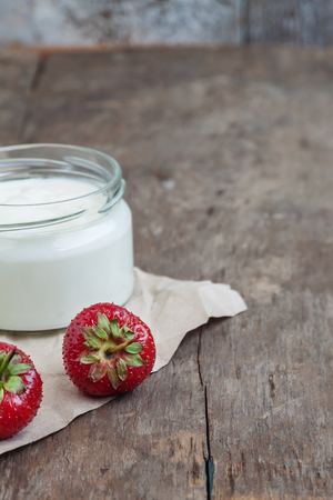 yoghurt in a glass and a bucket with fresh strawberries on a wooden background.の写真素材