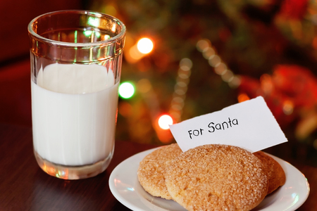 Christmas cookies and milk with note for Santa in front of lights of new year tree.の写真素材