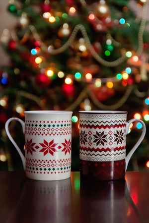 holidays, christmas, winter, food and drinks concept - close up of candy canes and cups on wooden table over lights.の写真素材