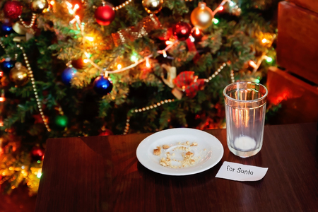 empty glass from milk and crumbs from cookies for Santa Claus under the Christmas tree with lights, close-up.の写真素材