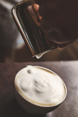 man pouring into a cup of coffee with milk.の写真素材