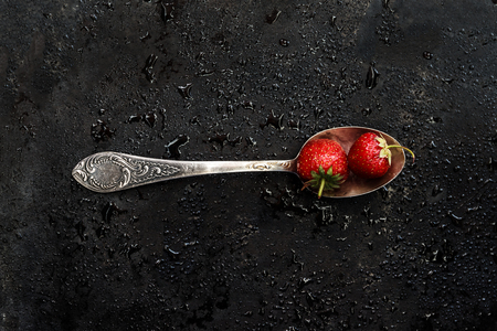 in a spoon a wet strawberry on a dark background with splashes of water, top view.の写真素材