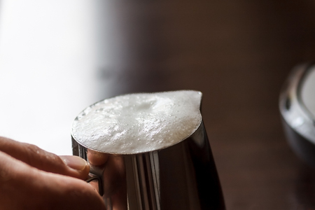in male hands milk jug with whipped milk, close-up.の写真素材