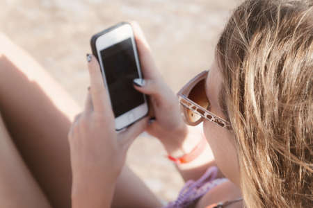 A young tanned woman looks into a smartphone through sunglasses on a lounger. The concept of a lifestyle is always on the Internet.の写真素材