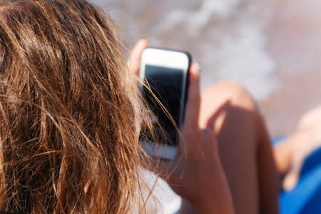 A young tanned woman looks into a smartphone through sunglasses on a lounger. The concept of a lifestyle is always on the Internet.の写真素材
