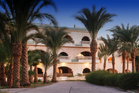 Palm trees and other landscaped trees on the background of a resort hotel in Egypt, Sharm el-Sheikh at sunset. Beautiful low one-two-storey houses-villasのeditorial素材
