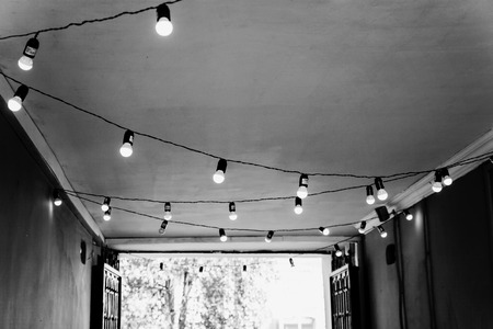 The ceiling in the street cafe is decorated with a garland with light bulbs. Monochrome black and white photography.の写真素材