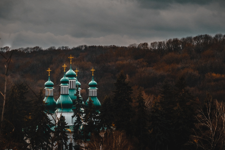The cathedral monastery with many crosses on several roofs can be seen on the mountain with autumn red-bard trees under a gloomy sky. Landscape.の写真素材