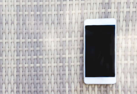 White smartphone lies on a wicker outdoor table. View from aboveの写真素材