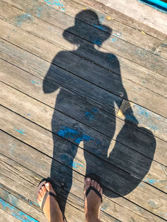 Top view, photo of bare feet and a pair of shadows on a wooden old floor. Photos on vacation, beach, summer.の写真素材