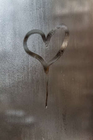 Drip in the shape of a heart on a misted window-glass. Close-up. Background.の写真素材