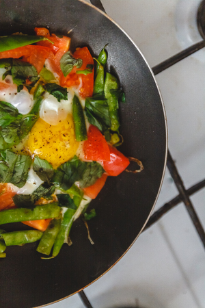 Fried eggs with vegetables and herbs in a pan, on the fire, on the stove, cook. Top view, close-up. Concept, healthy breakfast. Fly lay.の写真素材