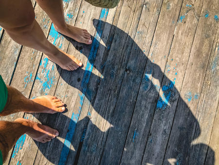 Top view, photo of bare feet and a pair of shadows on a wooden old floor. Photos on vacation, beach,...
