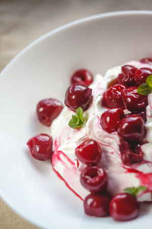 Cottage cheese cream and cream dessert with cherries and mint for breakfast on a white plate on a light background.の写真素材
