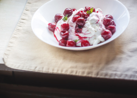 Cottage cheese cream and cream dessert with cherries and mint for breakfast on a white plate on a light background.の写真素材