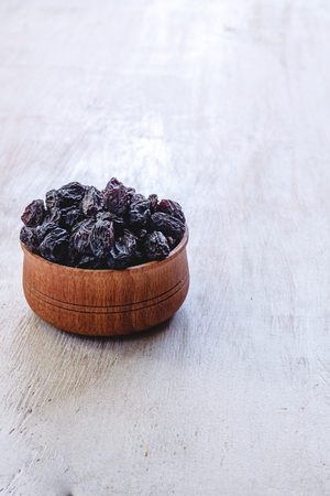 Dark blue raisins in a wooden bowl on a bright white background. Close-up. Insulatedの写真素材