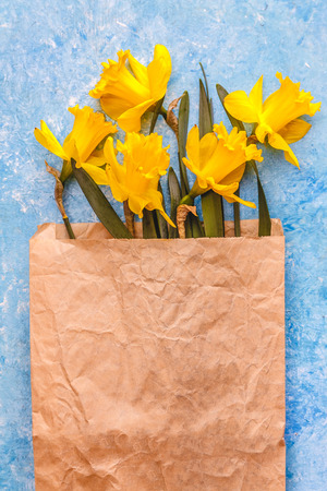 Flowers of daffodils are yellow on a blue marble background in a crafting paper bag, there is an empty space for text. Flat lay. View from above. Concept spring ecological natural holiday shopping.の写真素材