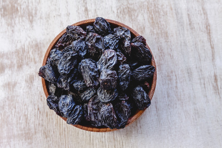 Dark blue raisins in a wooden bowl on a bright white background. Close-up. Insulatedの写真素材