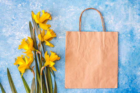 Narcissus flowers are yellow on a blue marble background and craft paper bag. Flat Lay. View from above. Concept spring ecological natural holiday shopping.の写真素材