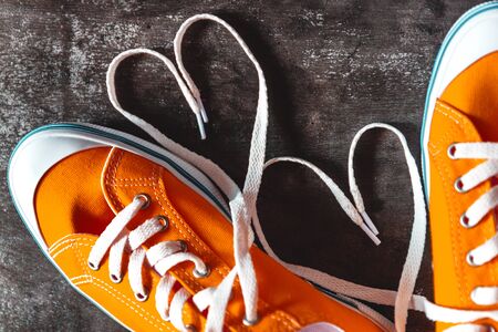 Yellow-orange sneakers on a grunge concrete dark background and a figure of a heart of laces. View from above. Close-up. Conceptの写真素材