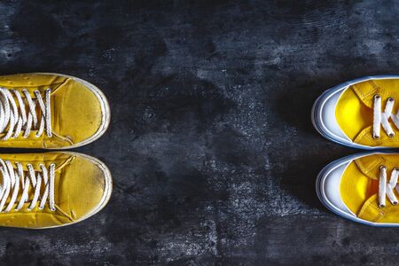 yellow old worn dirty torn sneakers and and new sneakers on a dark grunge background. top view. Copy spaceの写真素材