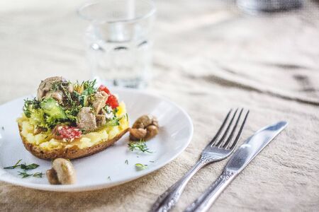 Whole baked potato with mushrooms, tomatoes and vegetables. Serving on a white plate on a light rustic fabric background. Close-up. Top view. Copy spaceの写真素材