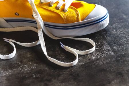 Yellow-orange sneakers on a grunge concrete dark background and a figure of a heart of laces. View...