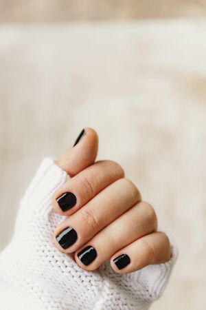 hand with black manicure on short nails in a white sweater on a light background. The concept of a stylish and warm winter.の写真素材