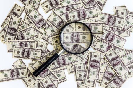 a lot of dollars banknotes on a white background and a magnifying glass on top, top view.
