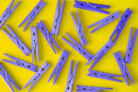 Wooden lilac-purple clothespins scattered on a yellow background. View from above. Copy space. Flat lay. The concept is natural, eco-friendly.の写真素材