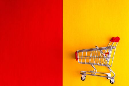 On a yellow-red background, a grocery cart-basket and a question mark. Flat lay, Top view, copy...