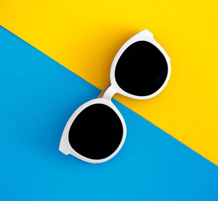 Sunny stylish white sunglasses on a bright blue-cyan and yellow-orange background, top view, isolated. Copy space. Flat lay.の写真素材