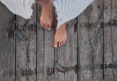 Beautiful female bare bare tanned legs with pink pedicure on wooden beach flooring. Top view, copy...