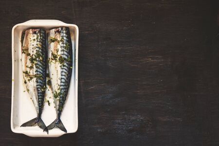 two raw fish mackerel in greens and herbs will be baked on a dark background. View from above. Retro effect.の写真素材