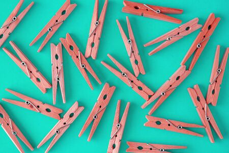 Wooden red clothespins are scattered on a blue-cyan-green background. Frame of clothespins. View...