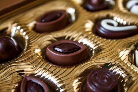 Chocolate candies of different shapes in a gold box, a perspective view and blur.
