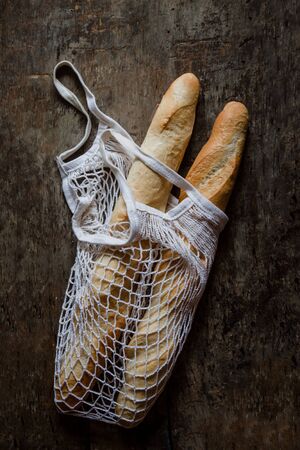 Fresh rosy baguettes in a string bag on a dark wooden retro background. Top view, copy space.