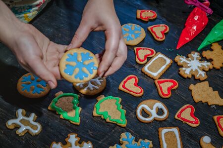 decorate Christmas gingerbread cookies using colored glaze on a dark wooden table, top view.