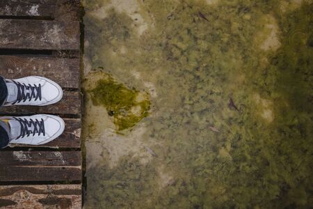 top view of female legs in white sneakers and jeans on the background of an old dirty autumn lake-river and a wooden platform. Copy space.の写真素材