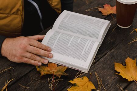 male female reads a book in autumn park drinks takeaway coffee coffee. Close-up over shoulder, blurred. top view, save space. Seen hands. In a dark retro style.の写真素材