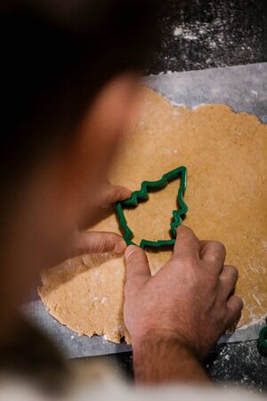male hands cut out gingerbread cookie in the form of a snowflake, Christmas tree, a man from raw...