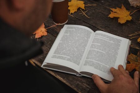 male female reads a book in autumn park drinks takeaway coffee coffee. Close-up over shoulder, blurred. top view, save space. Seen hands. In a dark retro style.の写真素材