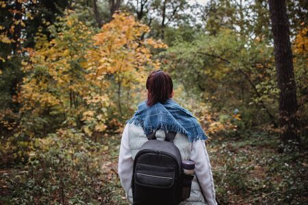 Hiking woman at autumn forest. Backpacker standing in woodland during fall season. Enjoying hike in nature at sunny day.の写真素材