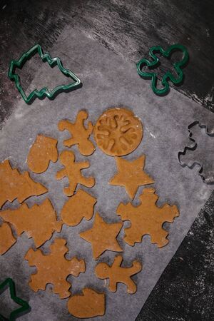 cut out gingerbread cookie in the form of a Christmas tree, star, little man, hearts from raw dough on parchment baking paper on a dark background. Top view. save space.の写真素材
