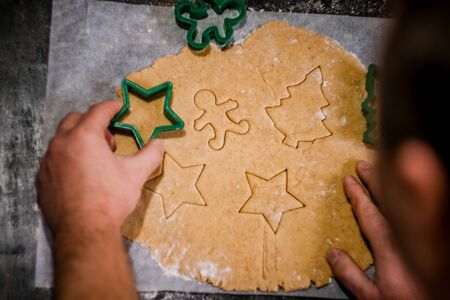 male hands cut out gingerbread cookie in the form of a snowflake, Christmas tree, a man from raw...