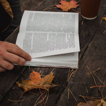 male female reads a book in autumn park drinks takeaway coffee coffee. Close-up over shoulder, blurred. top view, save space. Seen hands. In a dark retro style.の写真素材
