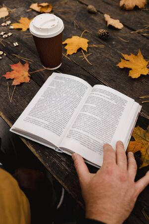 male female reads a book in autumn park drinks takeaway coffee coffee. Close-up over shoulder, blurred. top view, save space. Seen hands. In a dark retro style.の写真素材