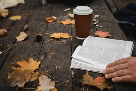male female reads a book in autumn park drinks takeaway coffee coffee. Close-up over shoulder, blurred. top view, save space. Seen hands. In a dark retro style.の写真素材