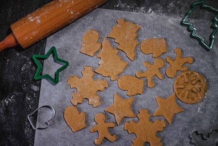 cut out gingerbread cookie in the form of a Christmas tree, star, little man, hearts from raw dough on parchment baking paper on a dark background. Top view. save space.の写真素材